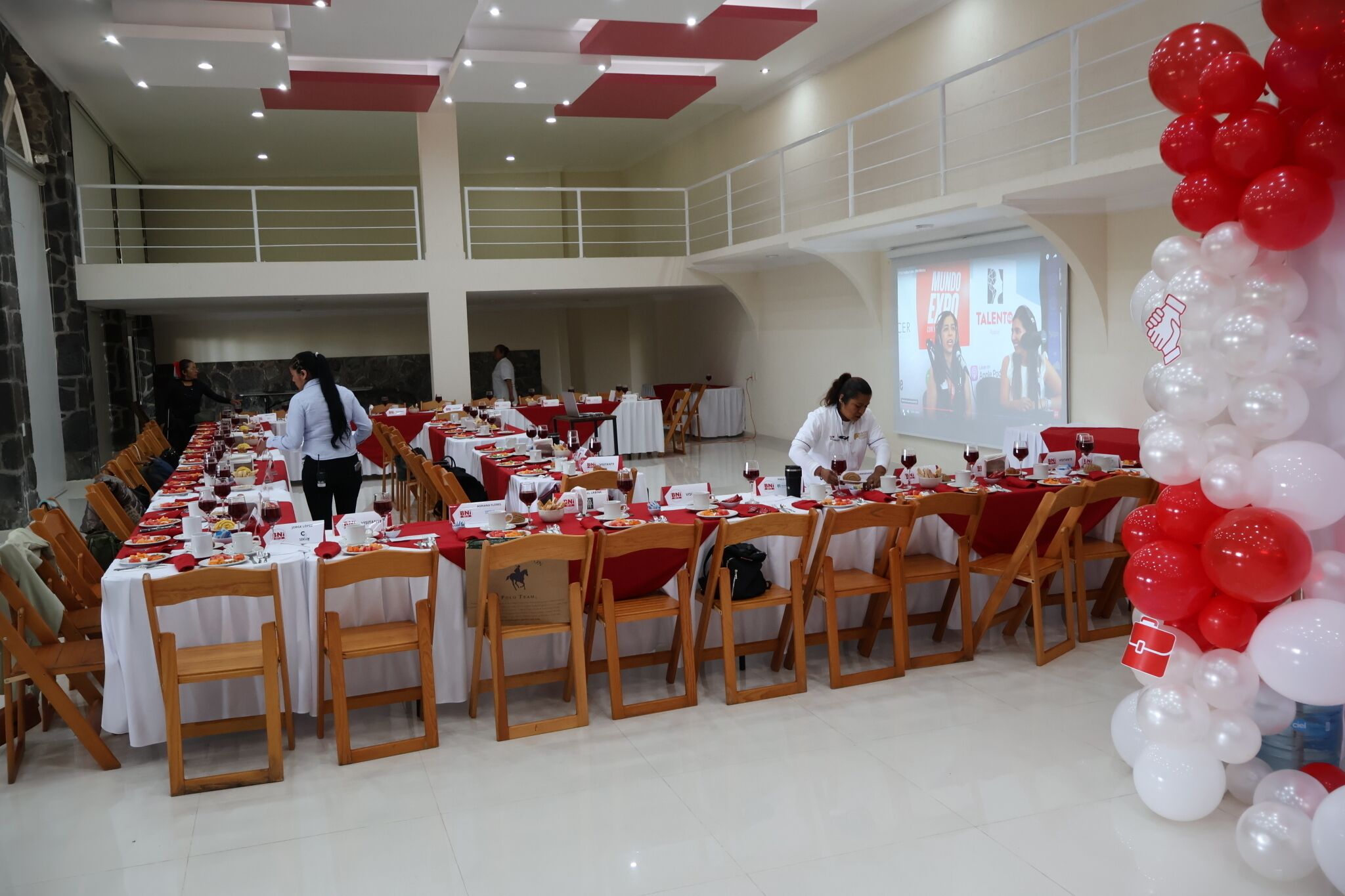A banquet hall with long tables, white tablecloths, and red and white balloons.