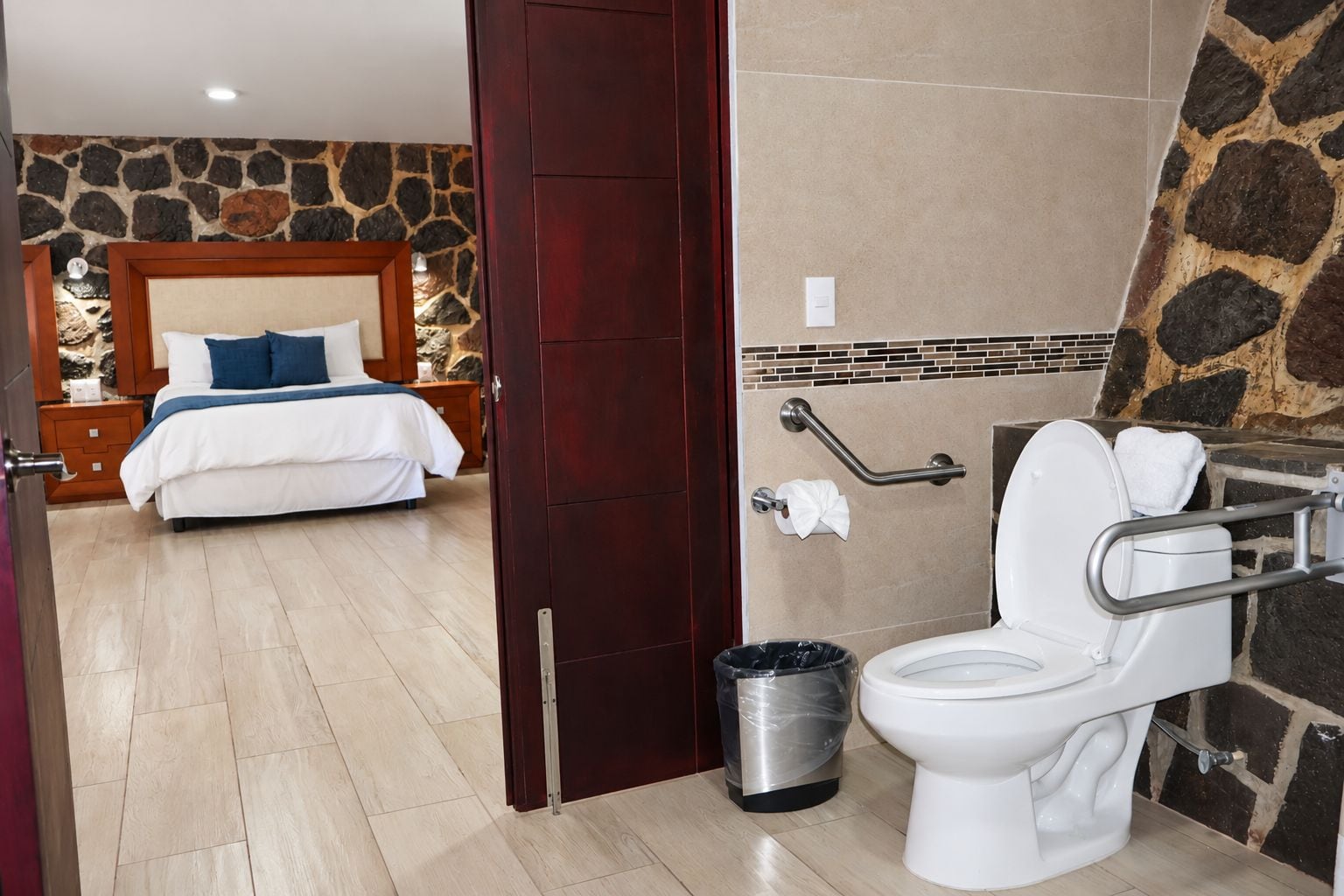 Una habitación de hotel con cama, baño con inodoro y un cubo de basura.