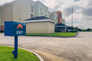 A building with an 'EXIT' sign, a parking lot, and a grassy area. - Suburban Studios Donaldsonville - Gonzales (Donaldsonville)
