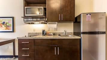 A compact kitchen with dark cabinets, a stainless steel refrigerator, a microwave, and a coffee maker.