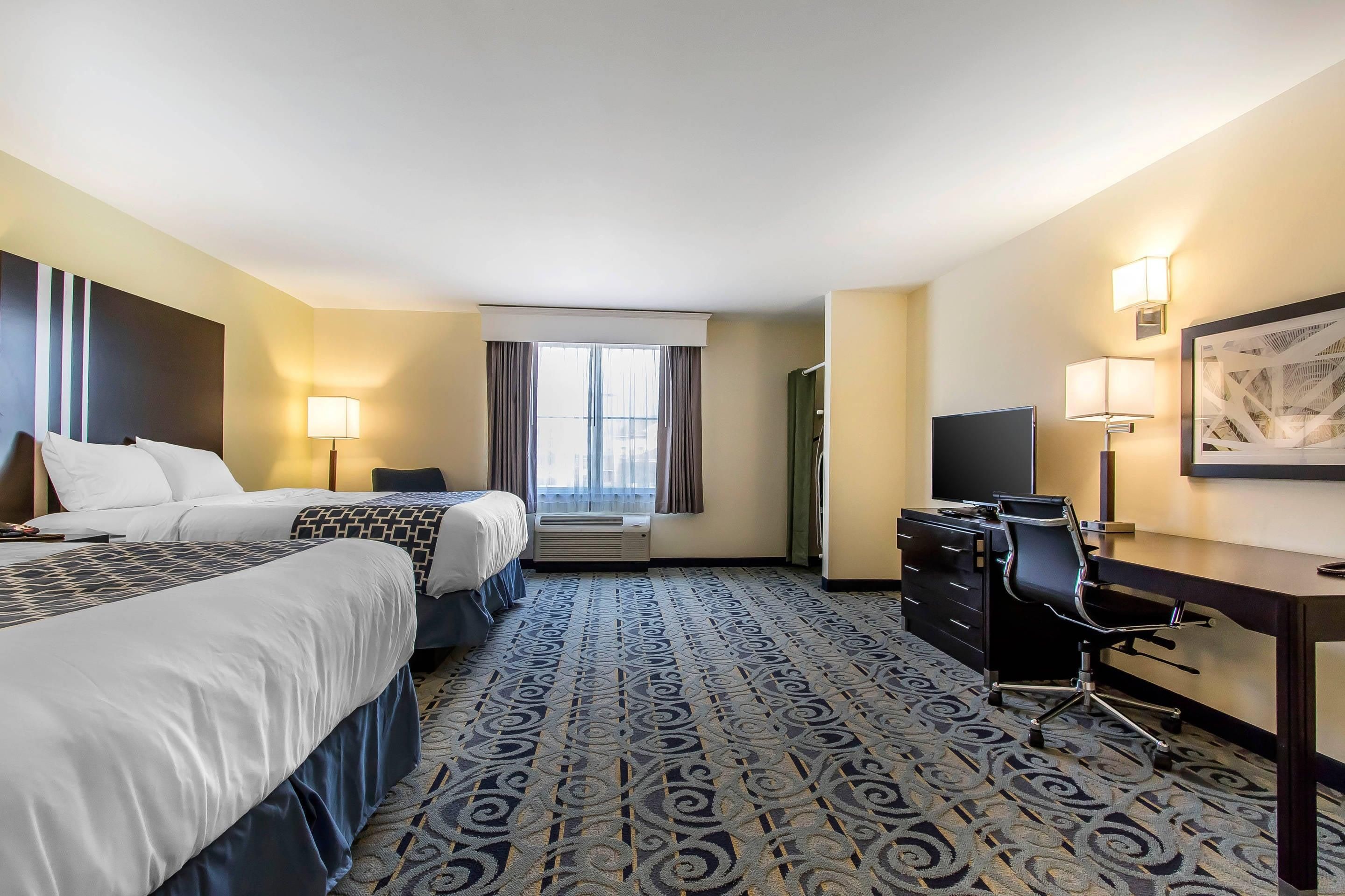 A hotel room with two beds, a desk, a chair, a TV, and a window with curtains.
