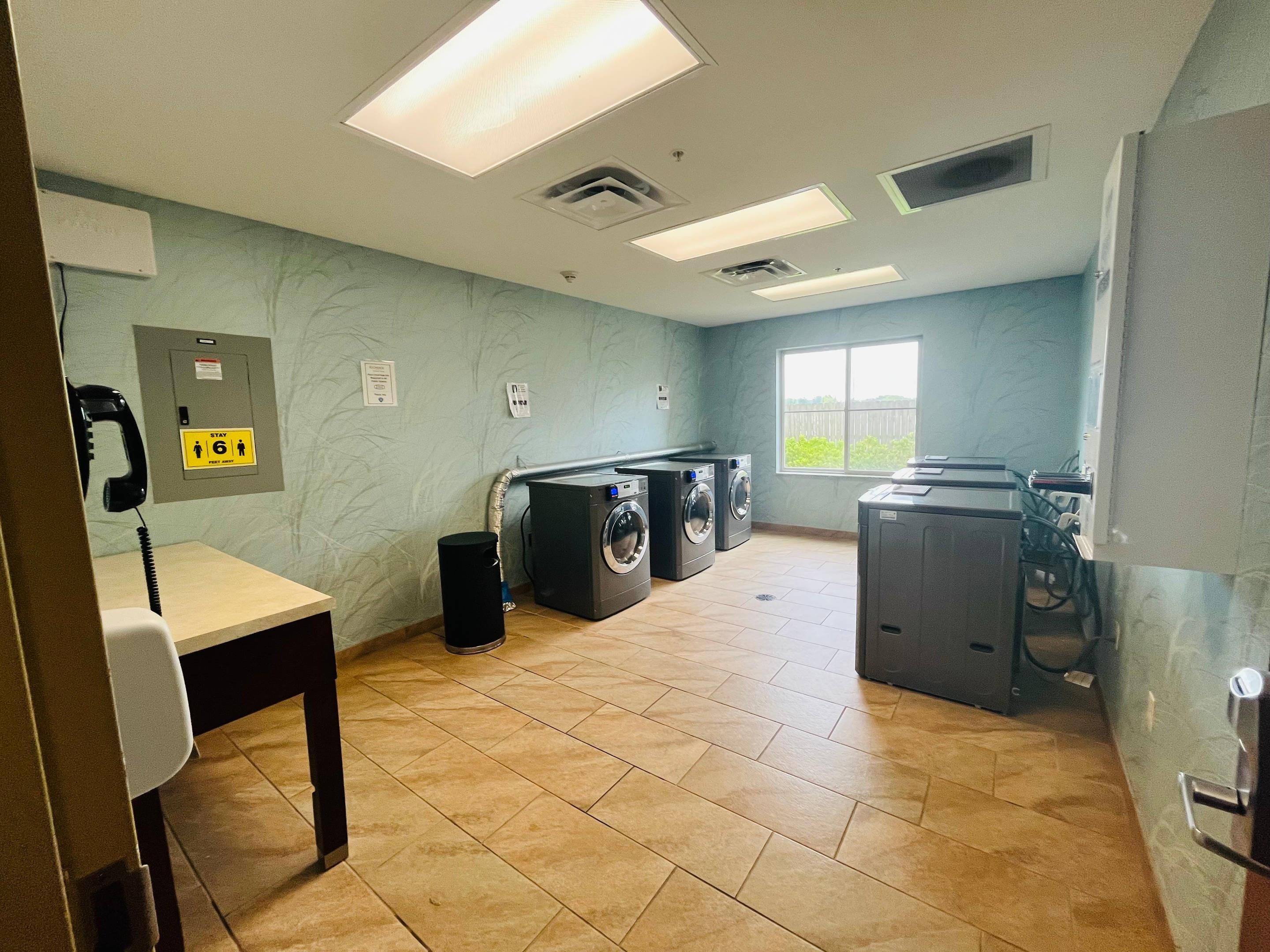 A laundry room with multiple washing machines, a telephone, and a window providing natural light.