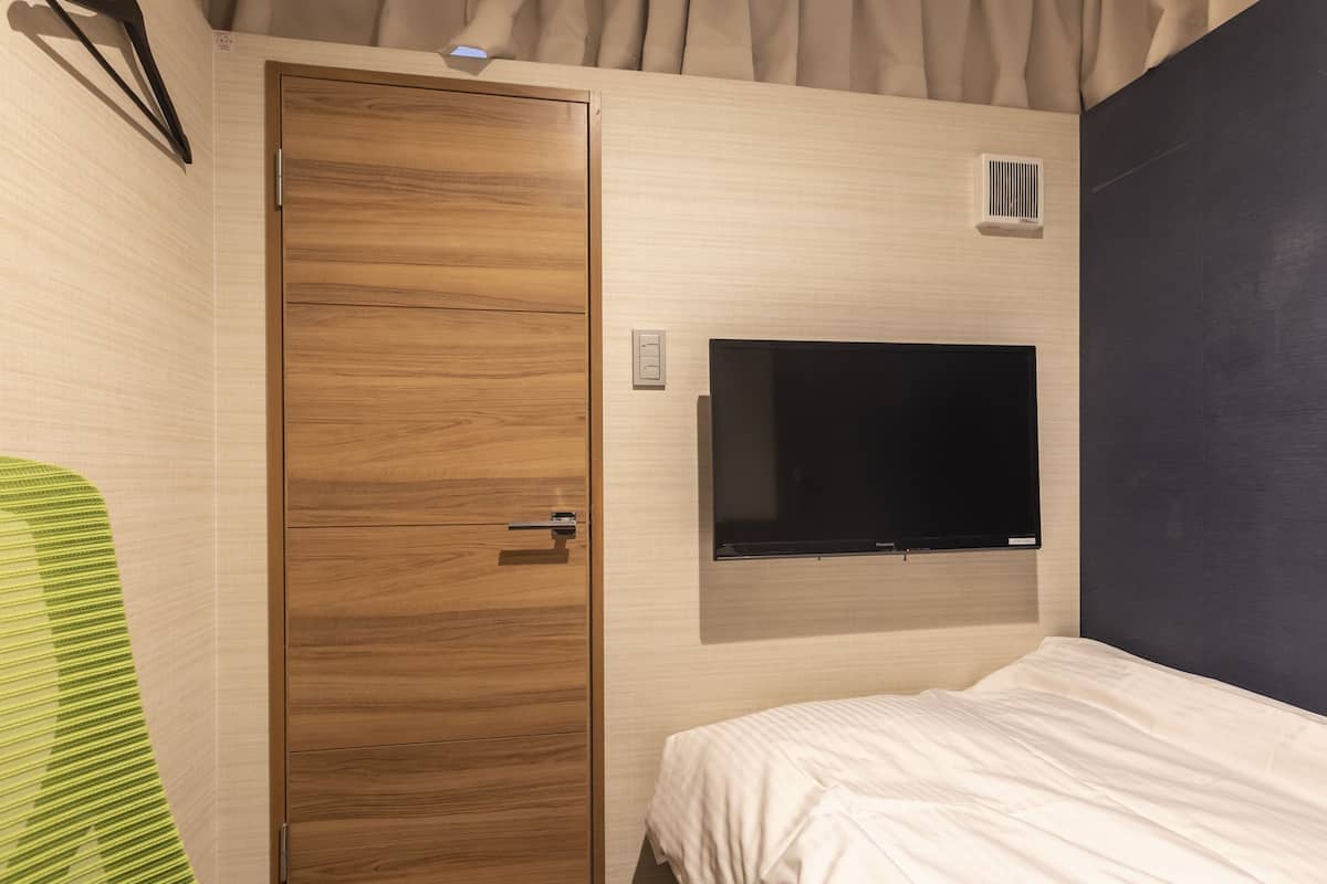 A modern hotel room with a wooden wardrobe, a flat-screen TV mounted on the wall, and a bed with white bedding.