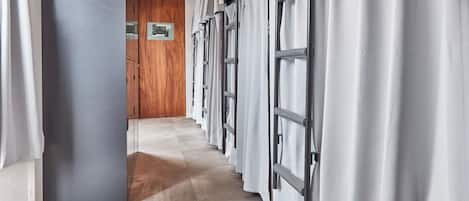 A corridor with a wooden door at the end, leading to a room with a large window and a framed picture on the wall.