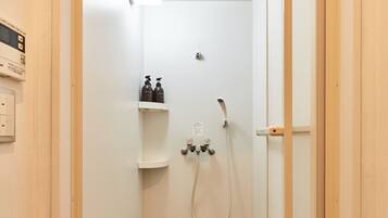 A small, narrow bathroom with a shower, a toilet, and a sink. There are two bottles of shampoo on a shelf above the sink.