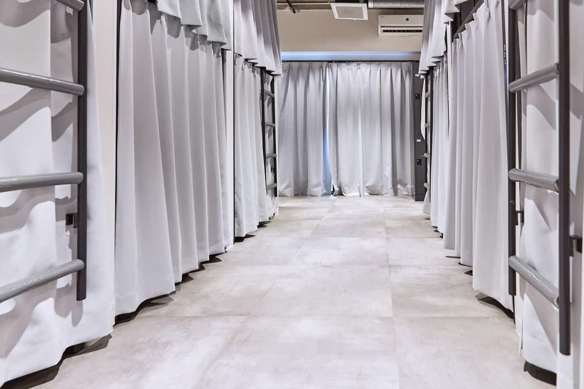A corridor with rows of white curtains and metal railings, leading to a door with a curtain.