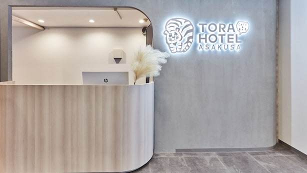A reception desk with a modern design, a logo for 'TORAHOTEL ASAKUSA', and a decorative plant. - Tora Hotel Asakusa - Hostel (Tokyo)
