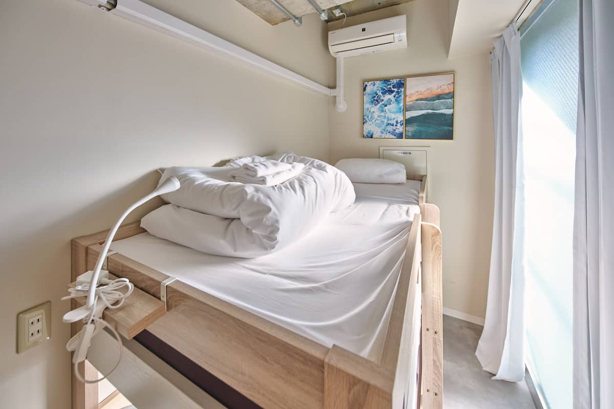 A single bed with white bedding, a power outlet, and a wall-mounted air conditioner.