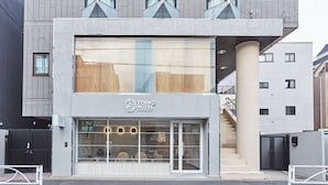 A modern hotel with a large glass facade, a visible staircase, and a prominent logo. - Tora Hotel Asakusa - Hostel (Tokyo)
