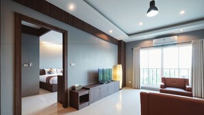 A modern hotel room with a large bed, a TV, a sofa, and a balcony with curtains. - Hansanan Hotel (Phitsanulok)