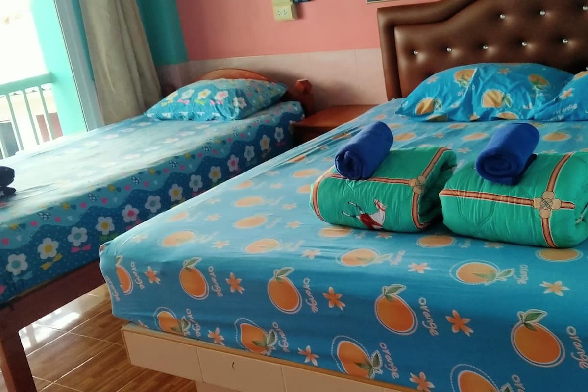 A hotel room with two beds, each with a blue floral bedspread and orange fruit patterns. There are rolled towels on the beds and a window with a view of the outside.
