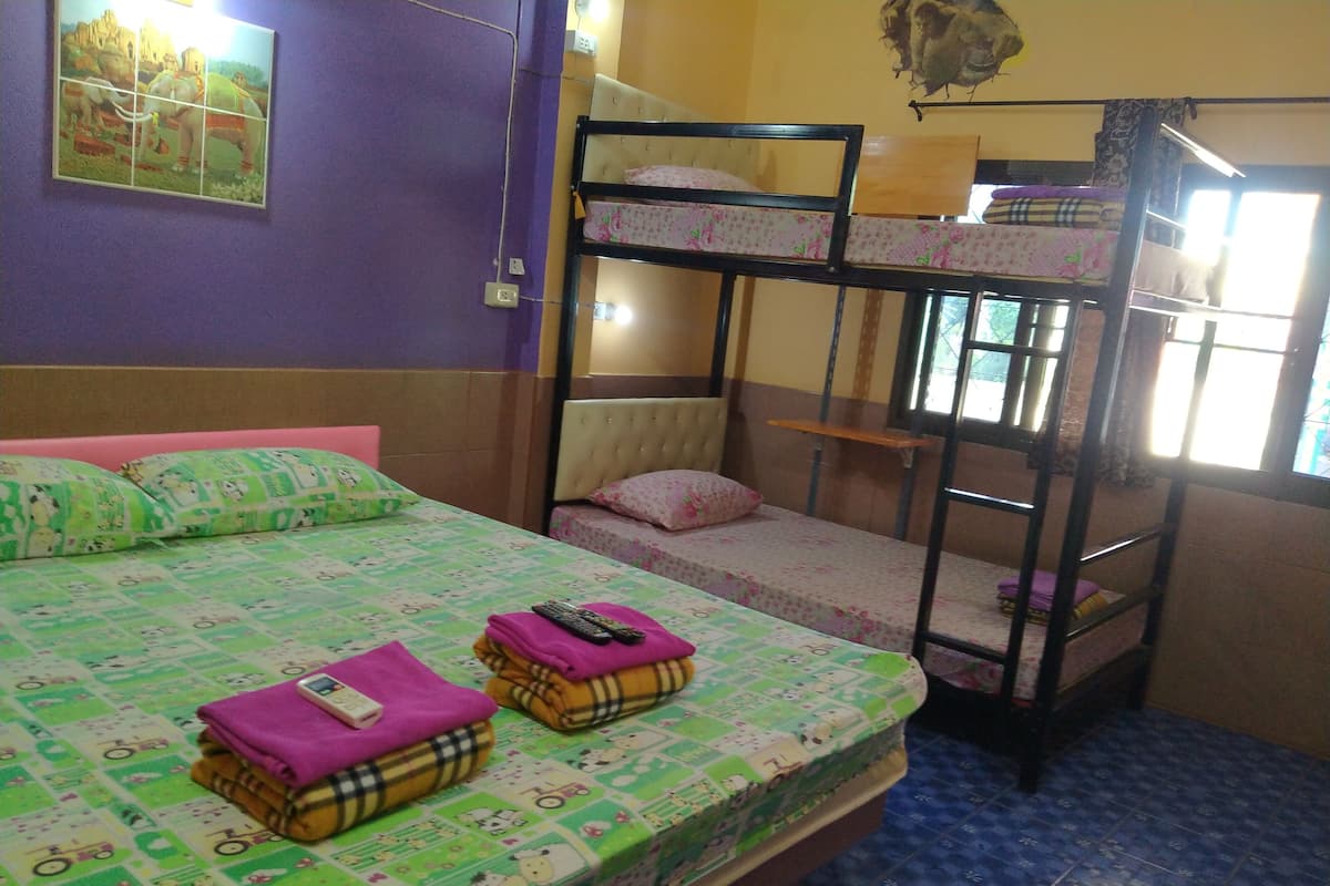 A bunk bed room with a green patterned bedspread, a purple pillow, and a pink pillow.