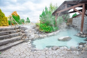 A stone-tiled hot spring area with steps leading into the water, surrounded by rocks and trees.