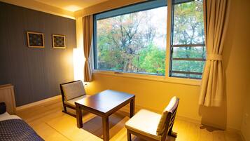 A room with a bed, a wooden table, two chairs, and a large window with curtains.