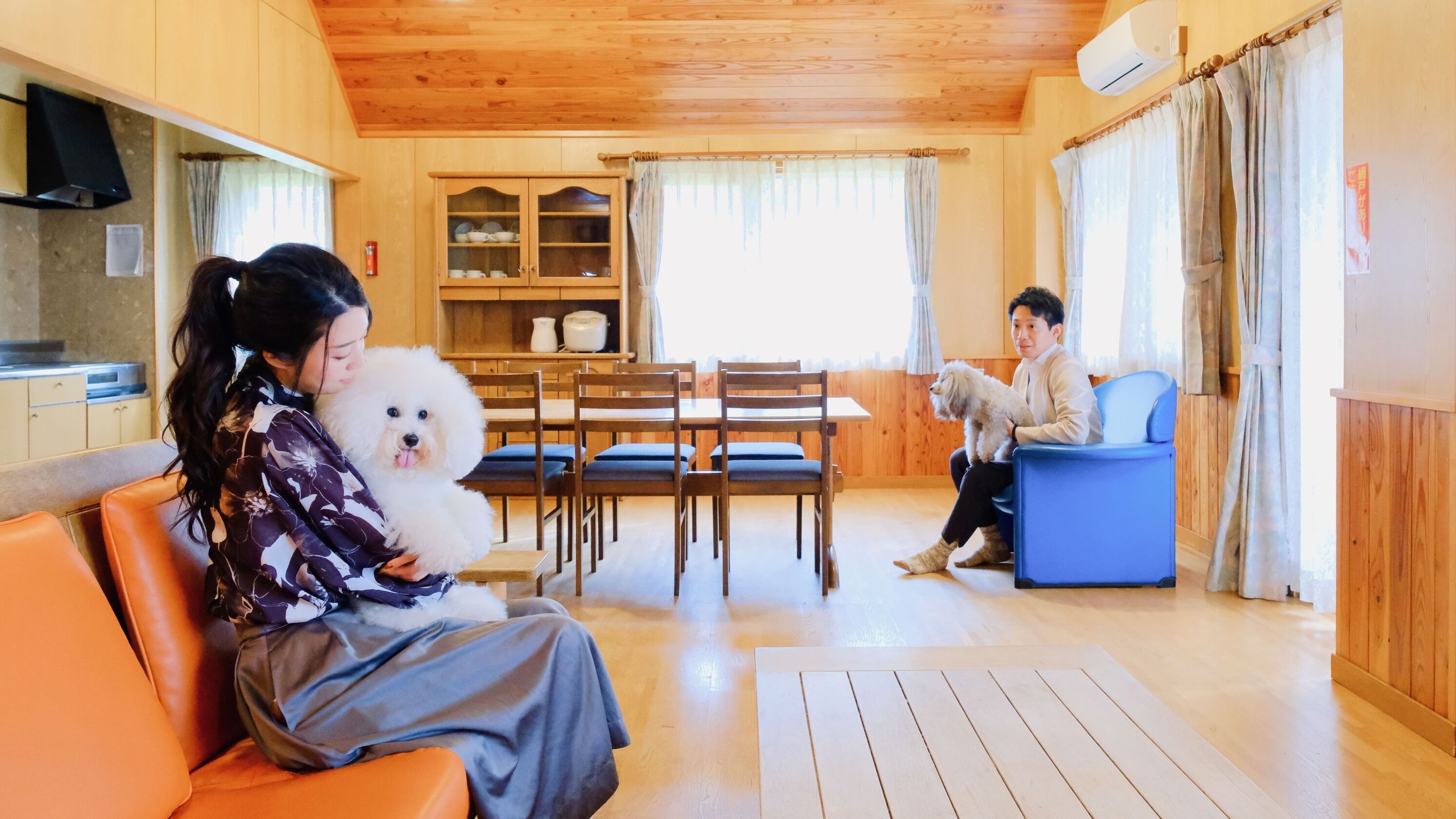 A cozy room with a wooden ceiling, a dining table with chairs, a sofa, and a blue armchair.