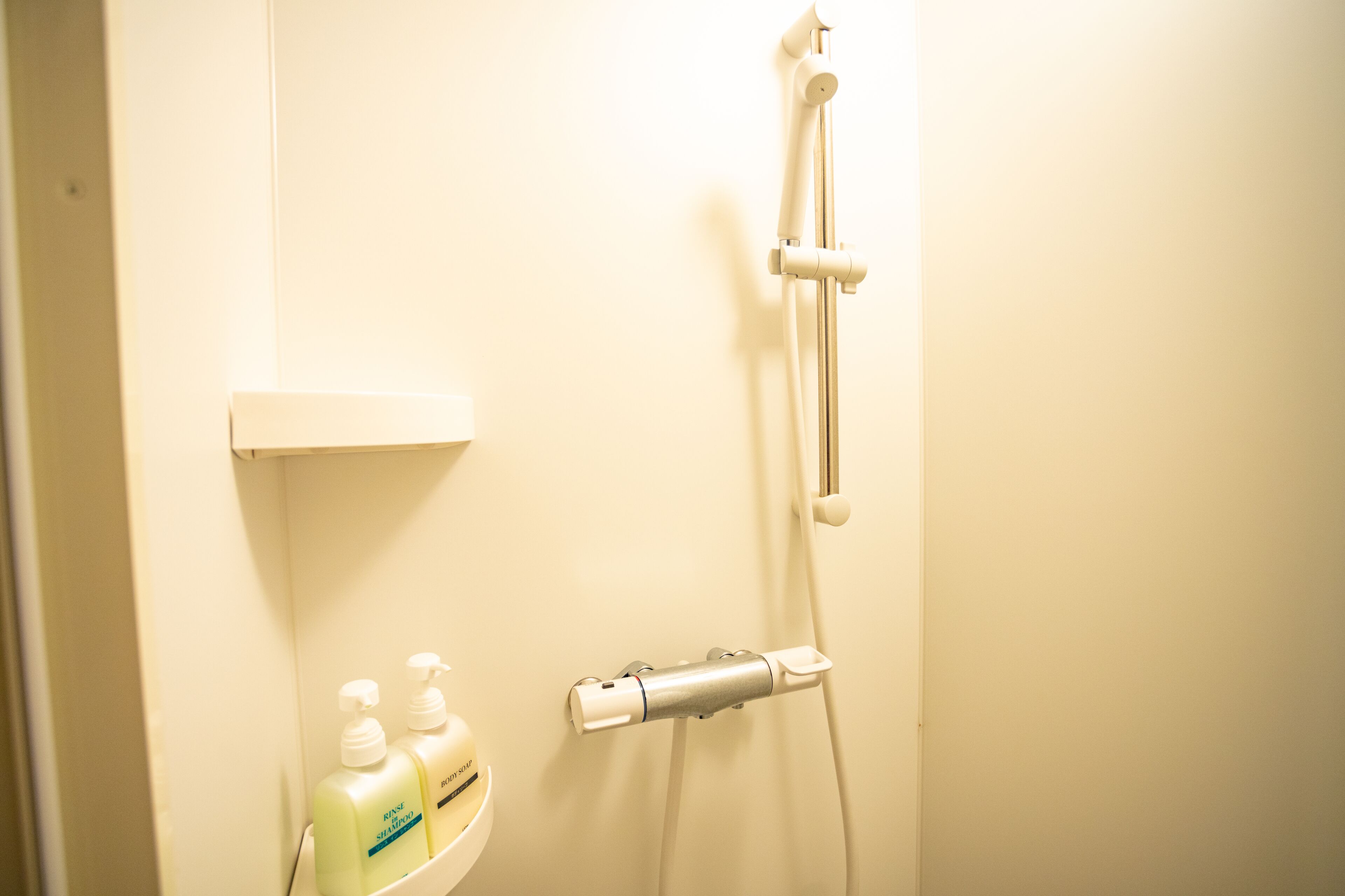 A bathroom with a shower, a soap dispenser, and a bottle of shampoo.