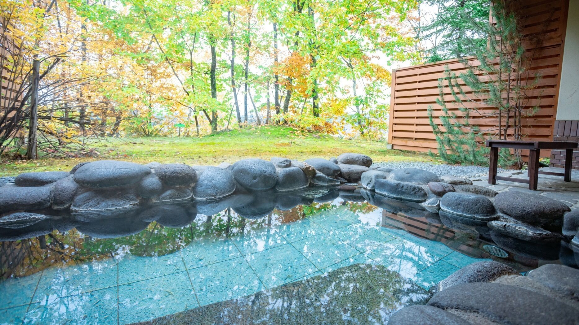 Un espacio al aire libre tranquilo con un estanque de piedra, una valla de madera y un banco.