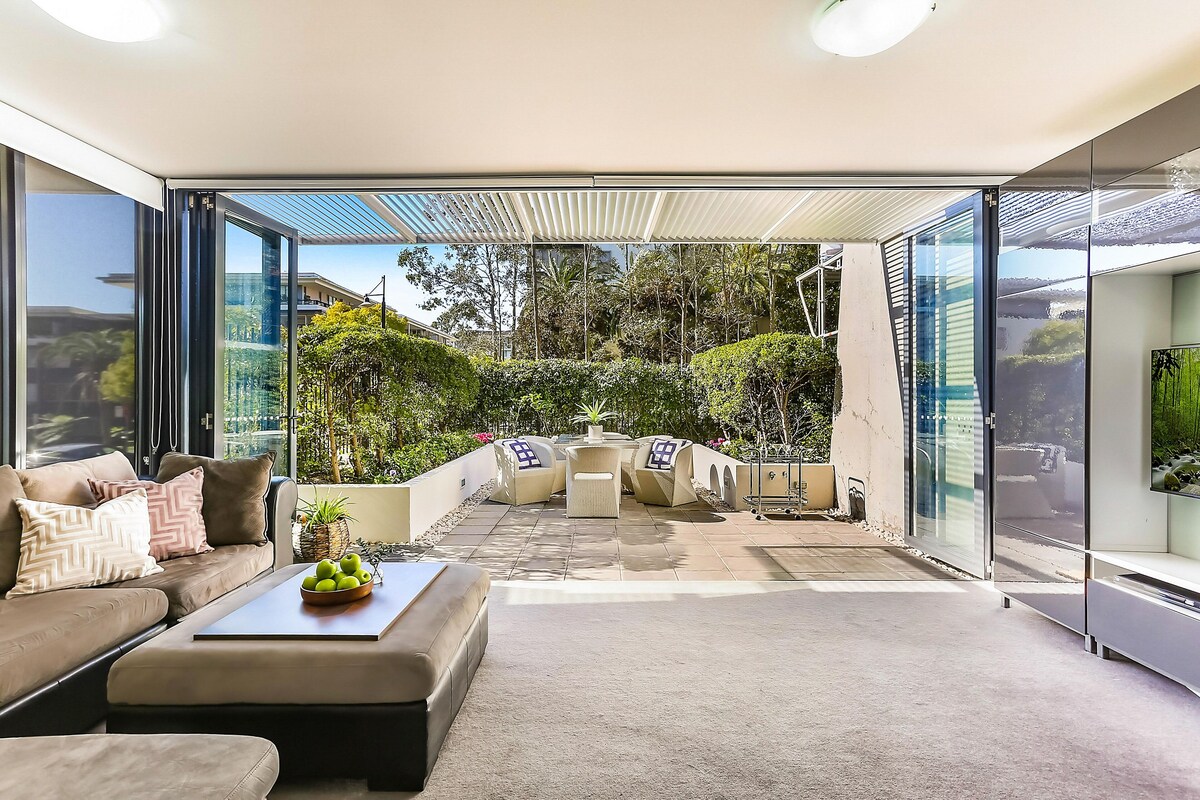 Un espacio al aire libre moderno con un sofá, un reposapiés y una mesa con fruta.