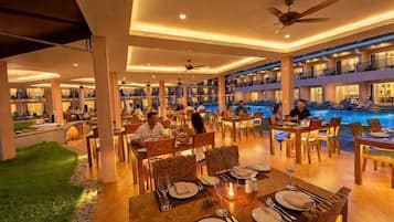 A spacious indoor dining area with multiple tables and chairs, a pool area with lounge chairs, and a view of the pool from the dining area.