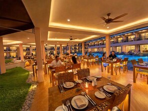 A spacious indoor dining area with multiple tables and chairs, a pool area with lounge chairs, and a view of the pool from the dining area. - Chivatara Resort & Spa Bang Tao Beach (Choeng Thale)