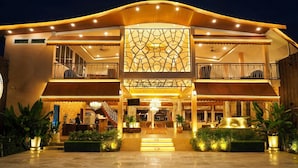 A hotel with a grand entrance, a central decorative wall, and a balcony on the upper floor.