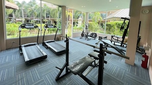 Ein Fitnessraum mit Laufbändern, einer Hantelbank und einem Ergometer, mit großen Fenstern und Blick auf einen Garten.