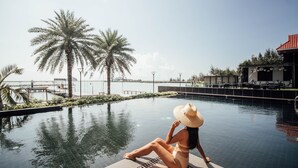 A woman sitting by a pool with palm trees and a view of the sea.