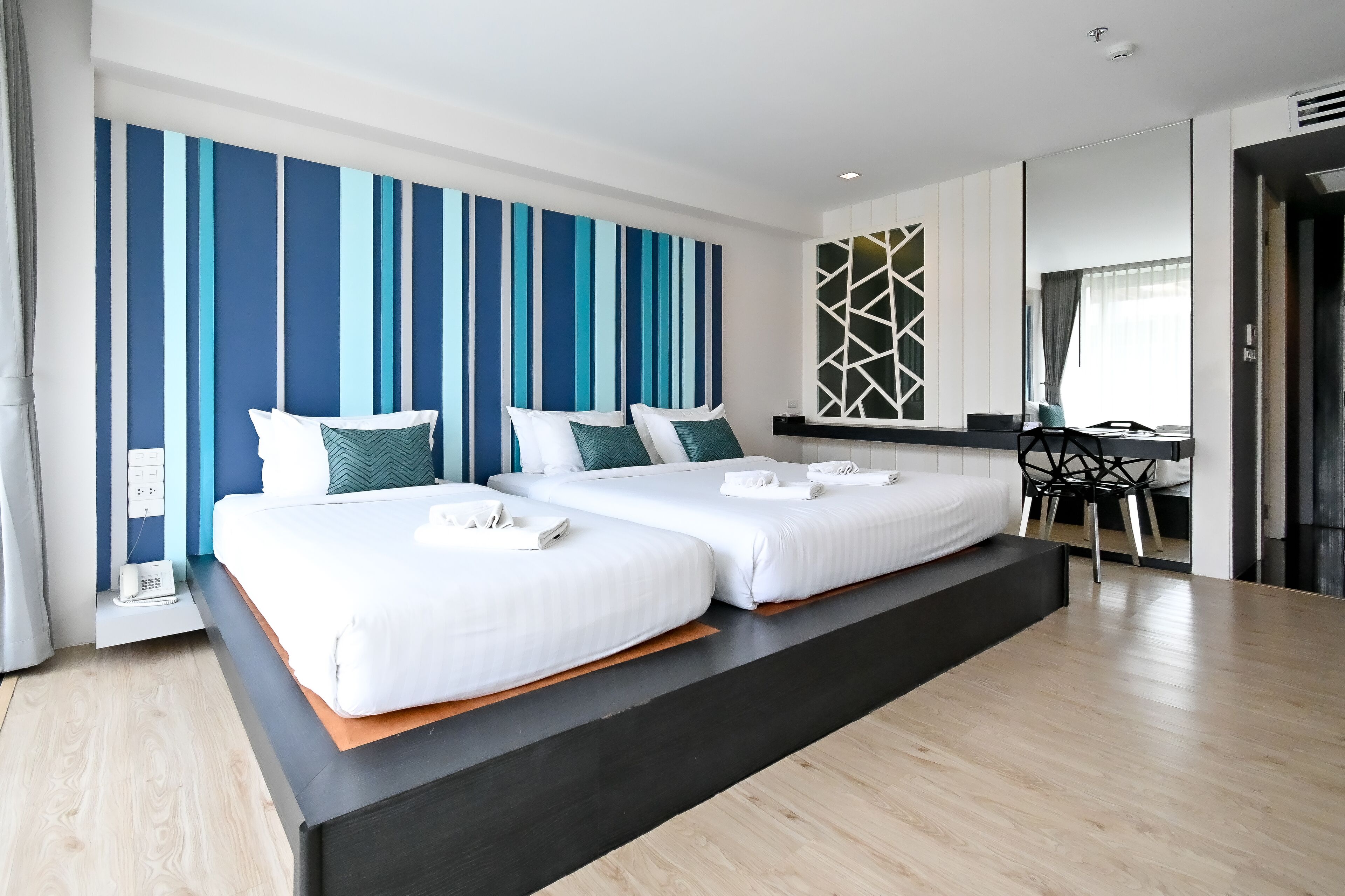A modern hotel room with two beds, a desk, and a chair.