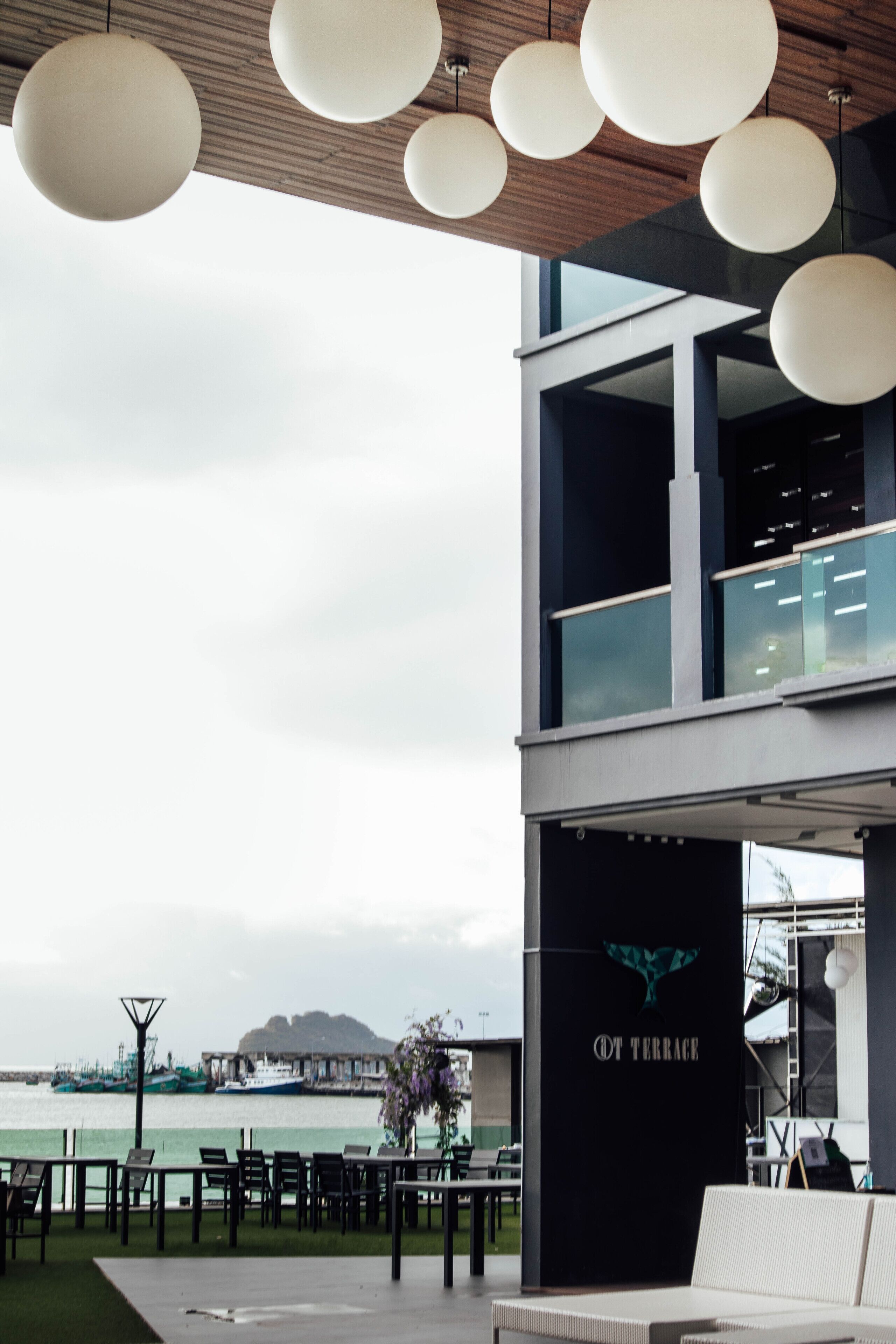 A modern outdoor seating area with a view of the water, a wooden ceiling, and a sign reading "OT TERRACE".