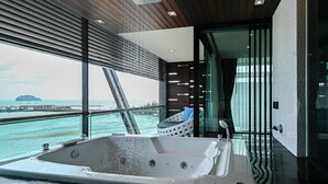 A modern bathroom with a large bathtub, a glass-enclosed shower area, and a view of the sea.