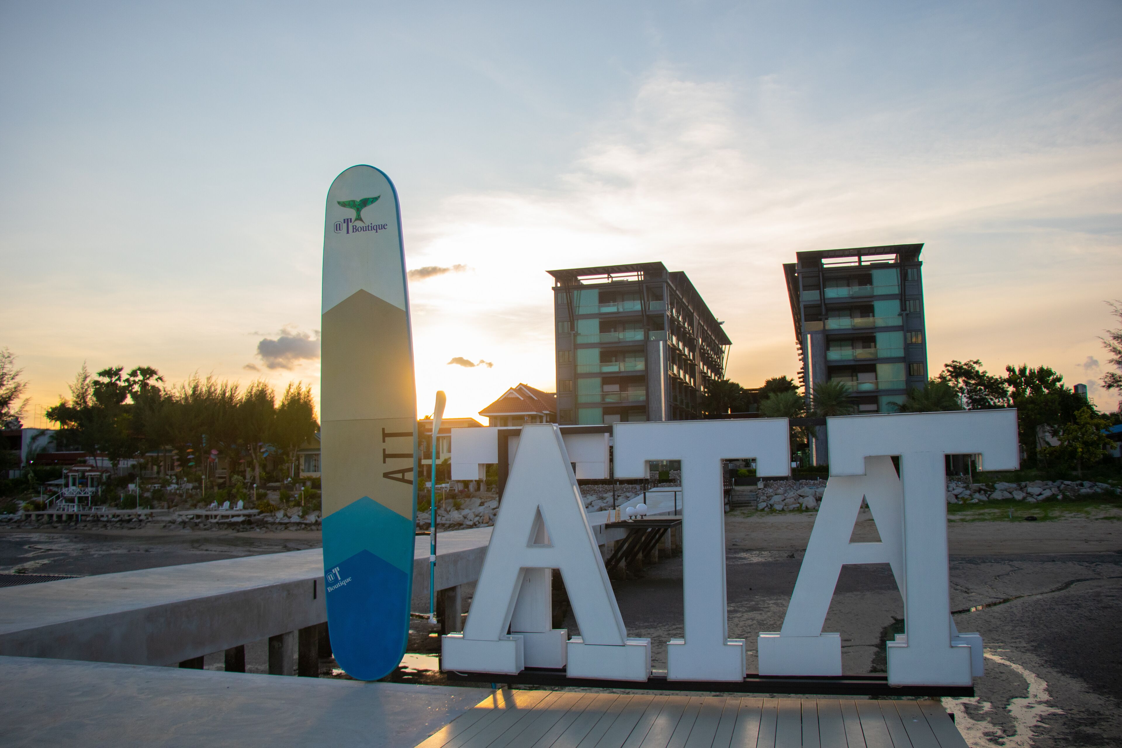 A large 'ATA' sign with a surfboard in front, set against a sunset background with modern buildings.