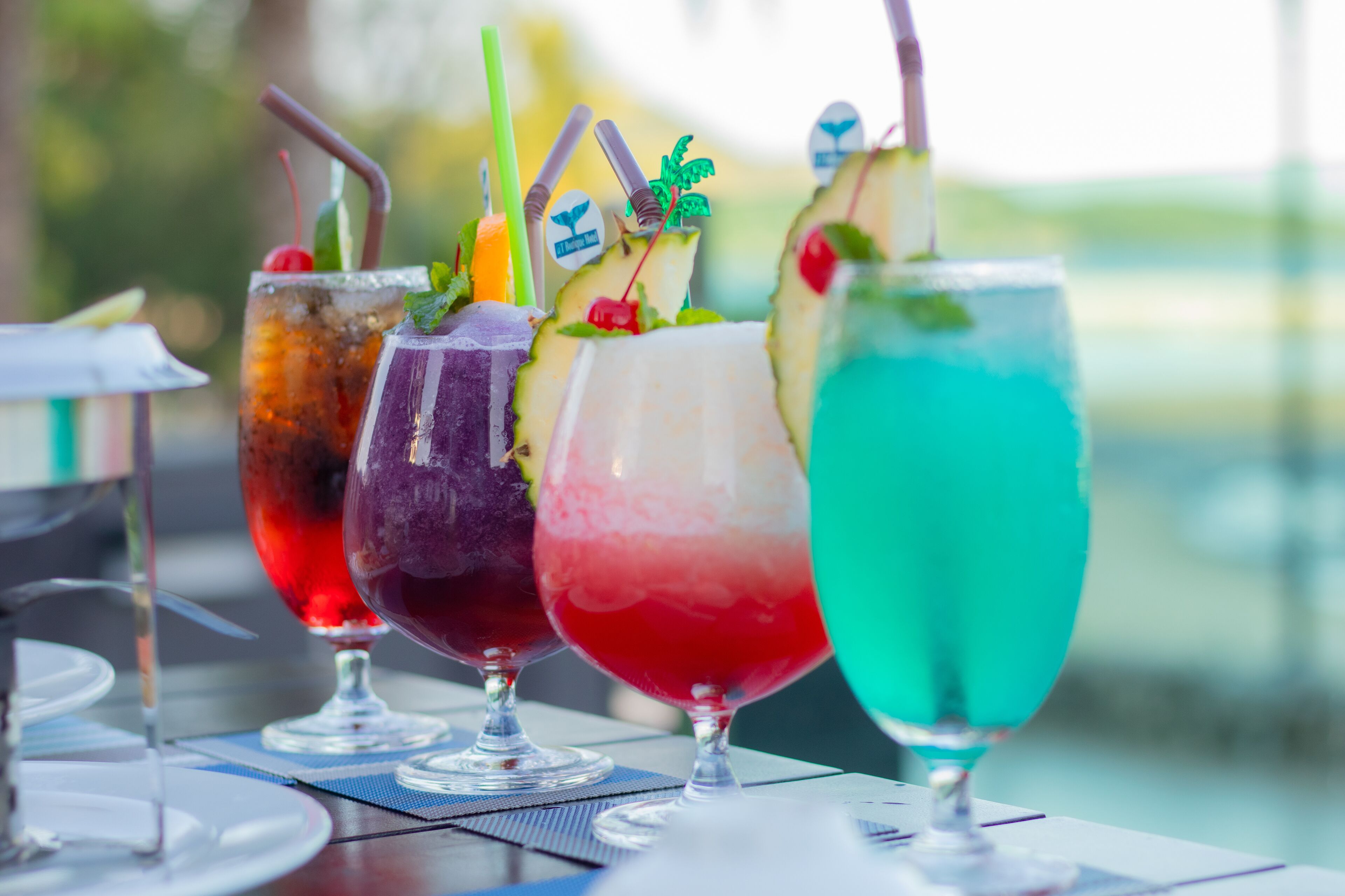 A row of colorful drinks on a table with clear glasses and various garnishes.