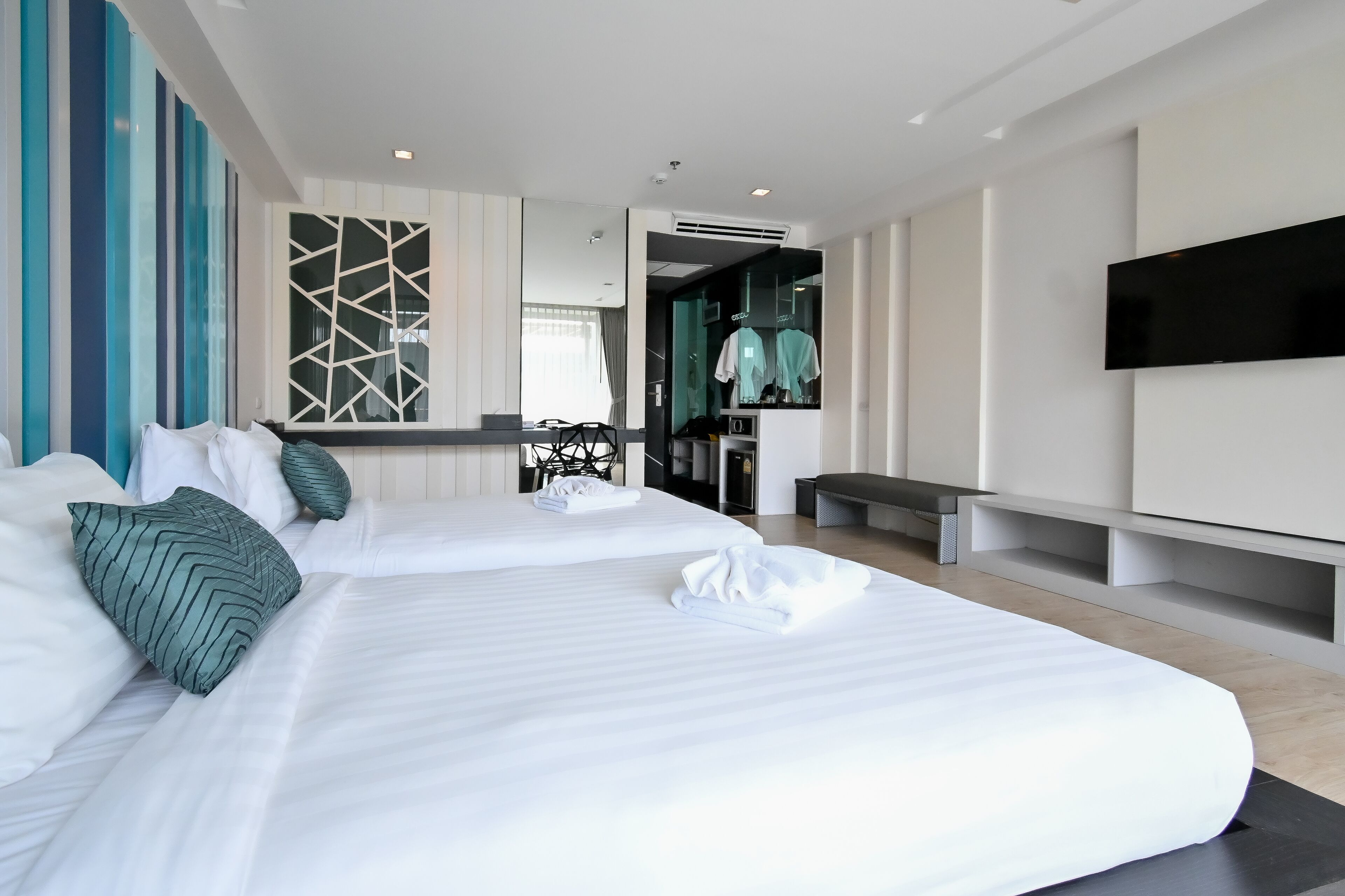 A modern hotel room with two large beds, a TV, and a walk-in closet.