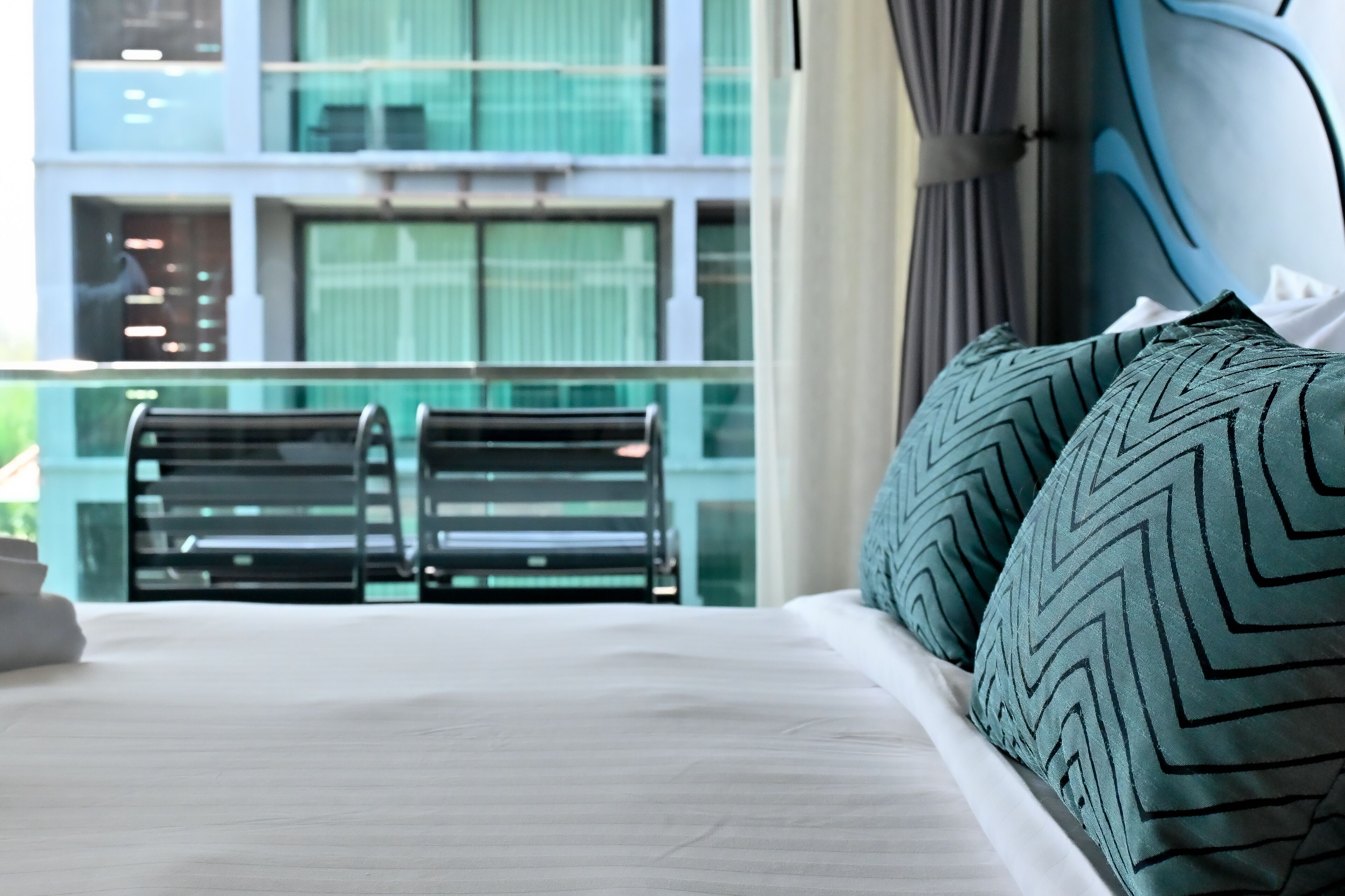 Hotellihuone, jossa on sänky, kaksi tuolia ja näkymä parvekkeelliselle rakennukselle.