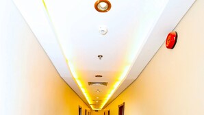 A long, narrow hotel corridor with a shiny tiled floor, recessed lighting, and a red emergency alarm on the wall. - Sea Shell Hotel (Manama)