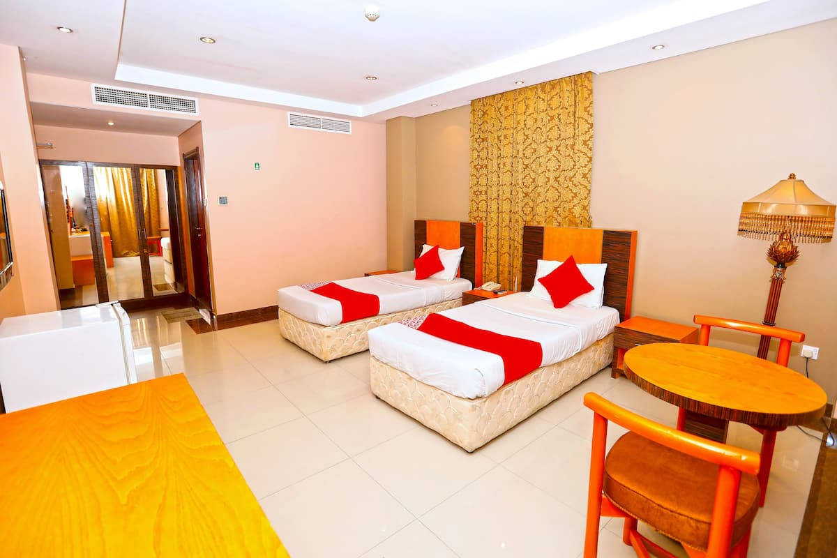 A hotel room with two beds, a small table, and a chair.