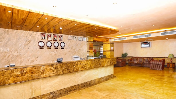 A hotel reception area with a marble counter, wooden ceiling, and a seating area with sofas. - Sea Shell Hotel (Manama)