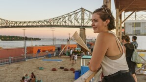A beach scene with a wooden structure, a bridge in the background, and people in the distance.