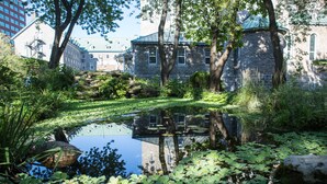 A stone building with a pond in front, surrounded by greenery.