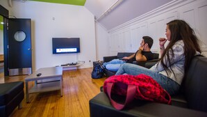 A modern living room with a flat-screen TV mounted on the wall, a wooden floor, and a black couch.
