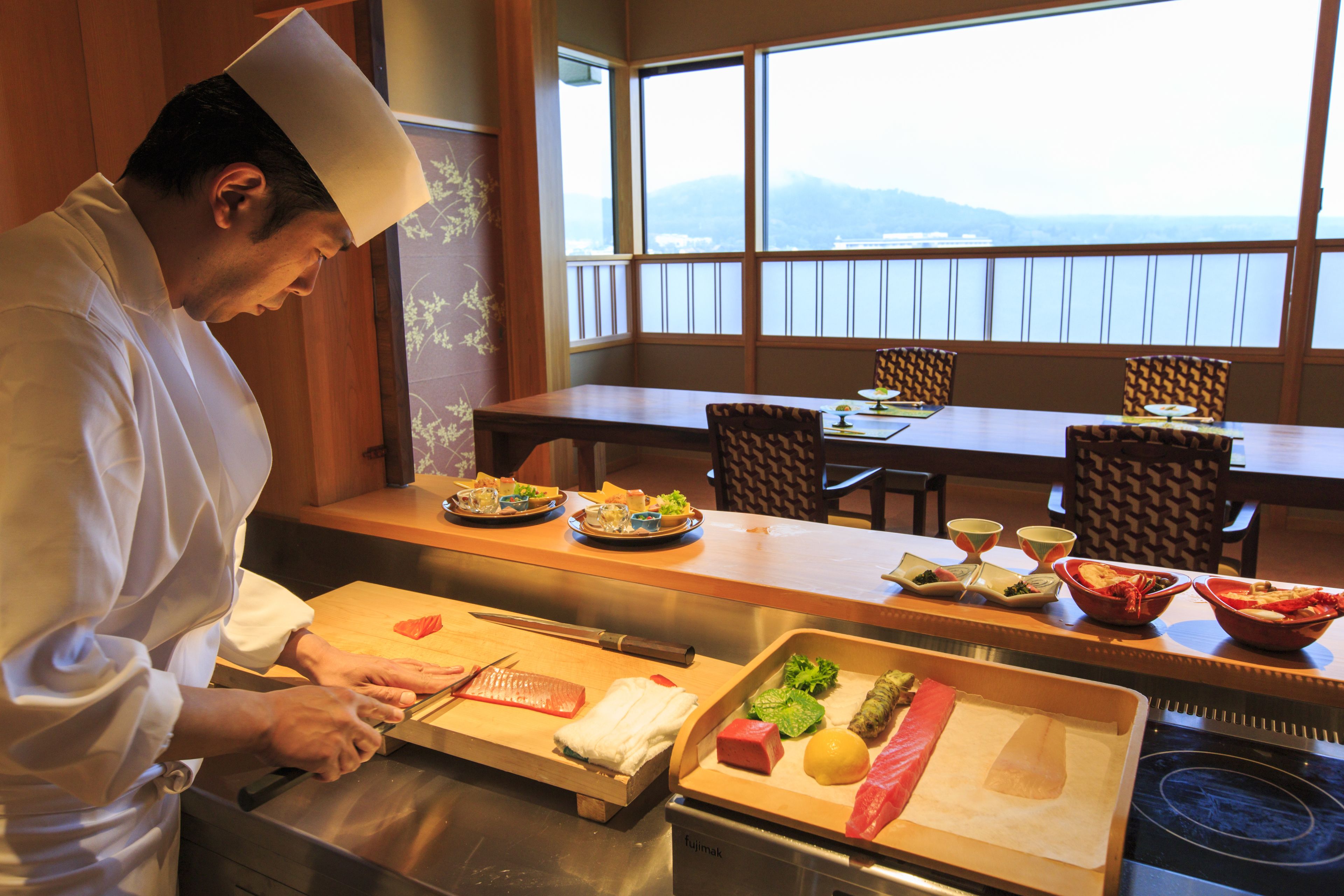 A chef preparing food at a counter with a view of the mountains through large windows.