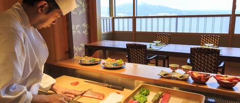 A chef preparing food at a counter with a view of the mountains through large windows.