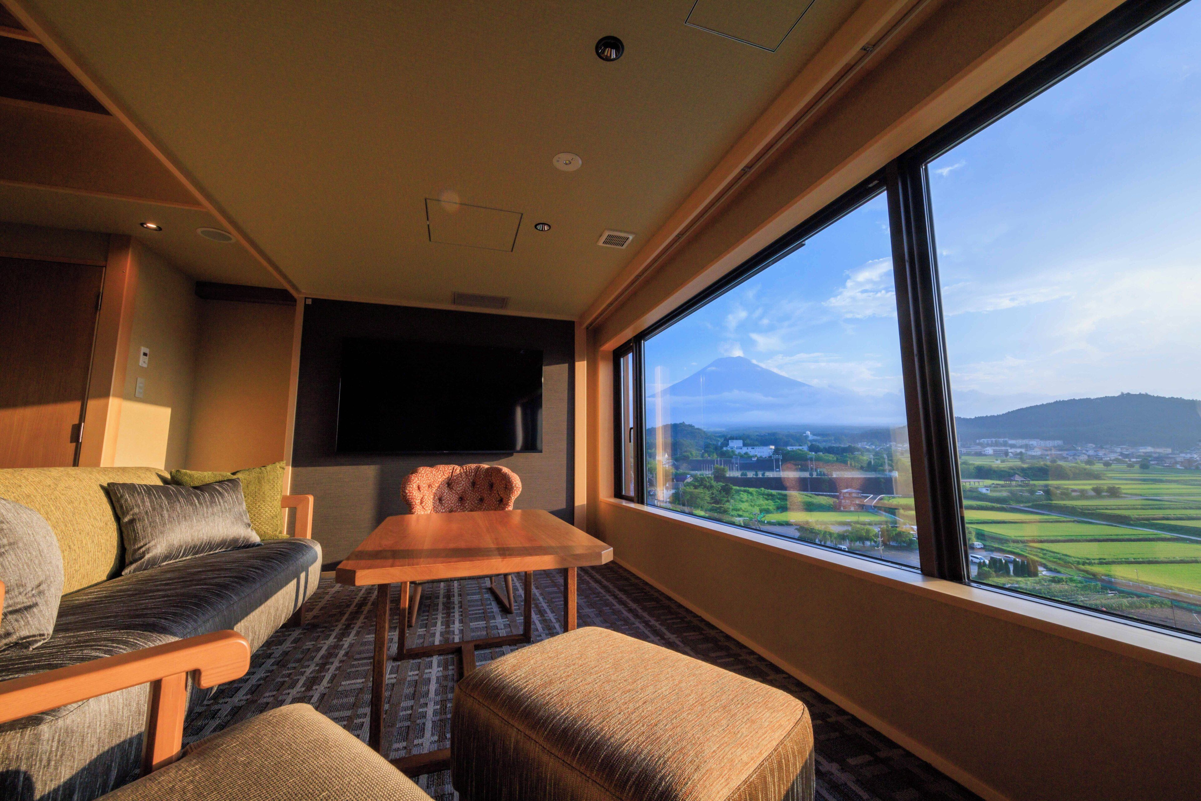 A room with a sofa, a table, and a large window offering a view of a landscape with a mountain.