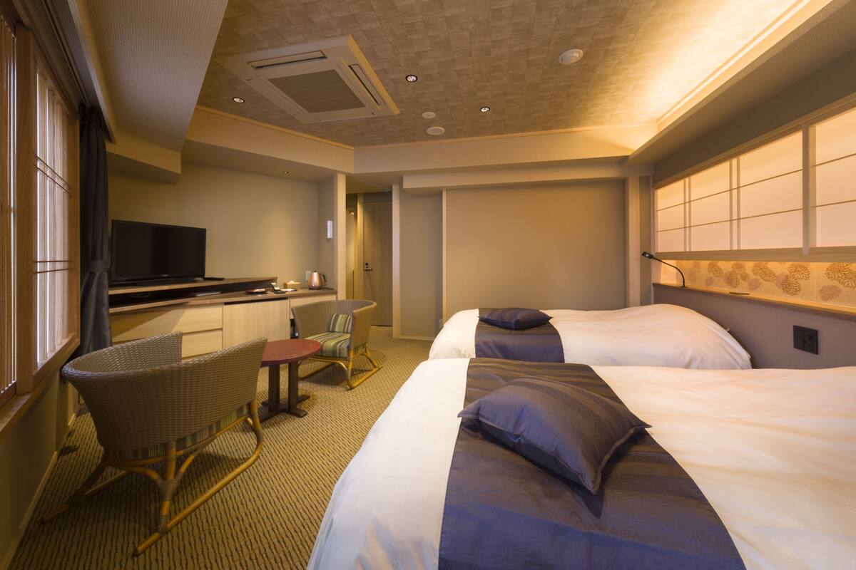 Ein Hotelzimmer mit zwei Betten, einem Fernseher, einem kleinen Schreibtisch und einem Stuhl.