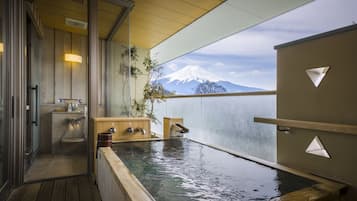 Relax in a serene onsen bath area with a rectangular bath, wooden bench, and stunning mountain views.