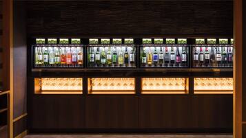 Zona de bar amb nombroses amples d'ampolles de begudes i una estant inferior amb gots penjats.