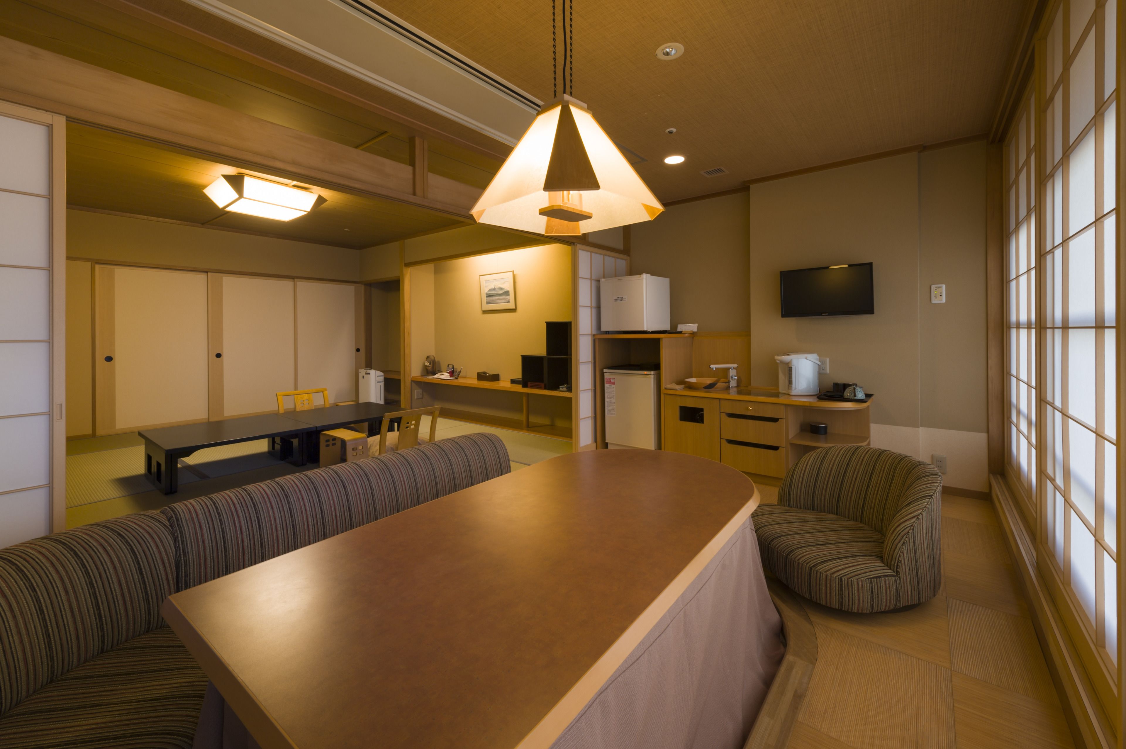 A modern hotel room with a dining area, a sofa, a TV, and a large window.