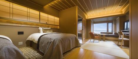A modern bedroom with two beds, a desk, and a view of the city.