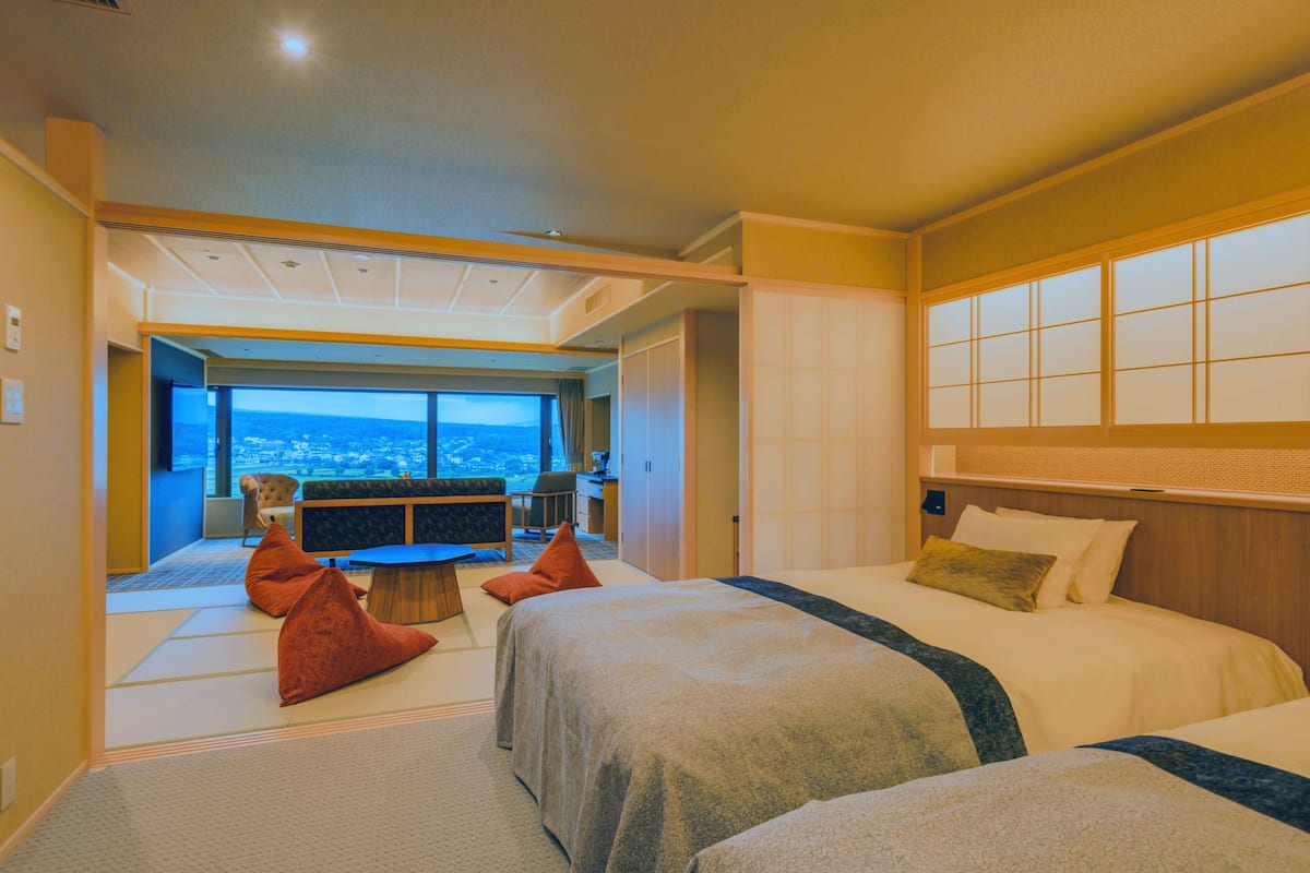 Ein Hotelzimmer mit zwei Betten, Blick auf die Stadt, einer Essecke und einem großen Fenster.