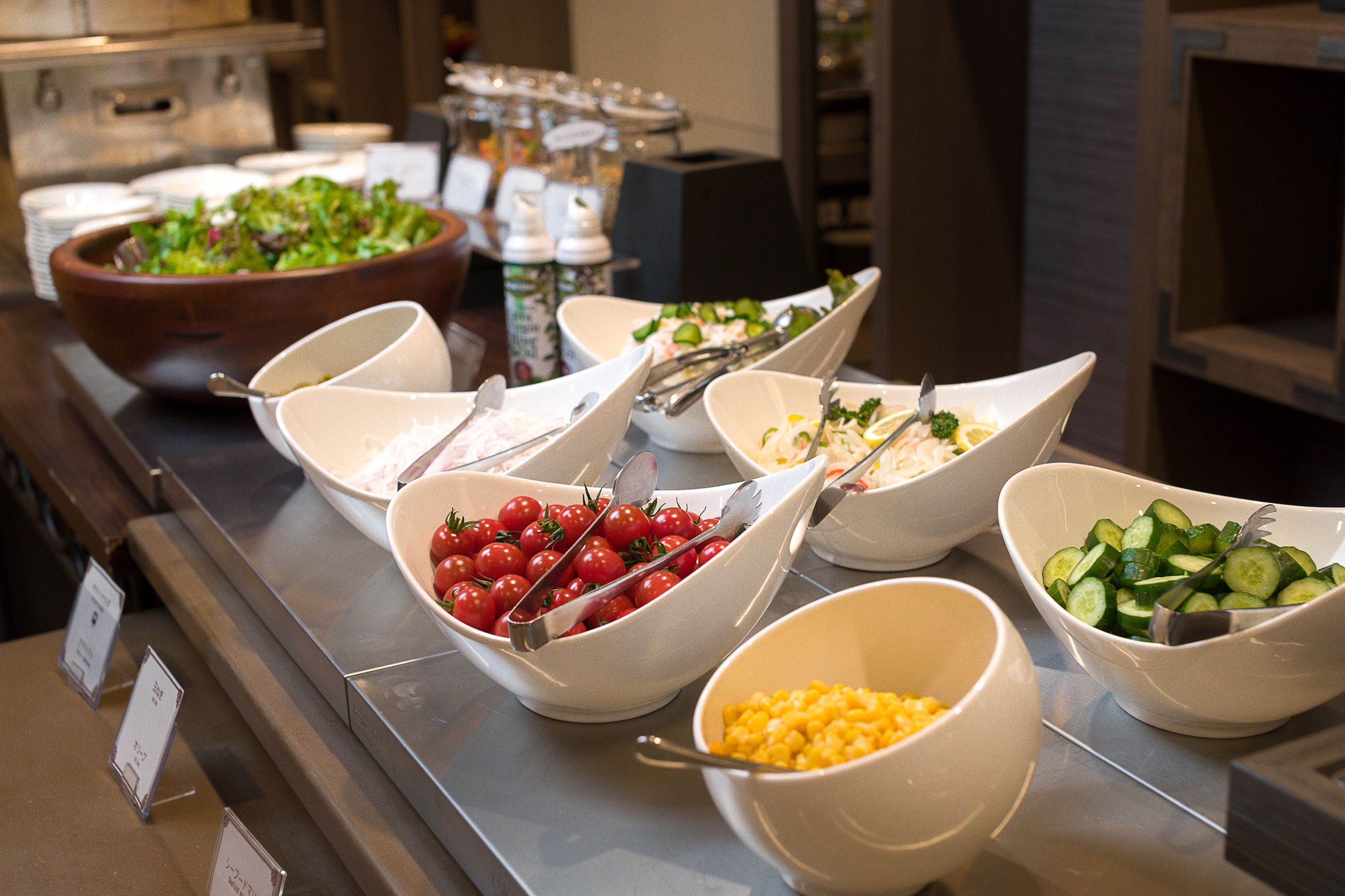Een buffet met diverse gerechten, waaronder salades, tomaten, komkommers en maïs.